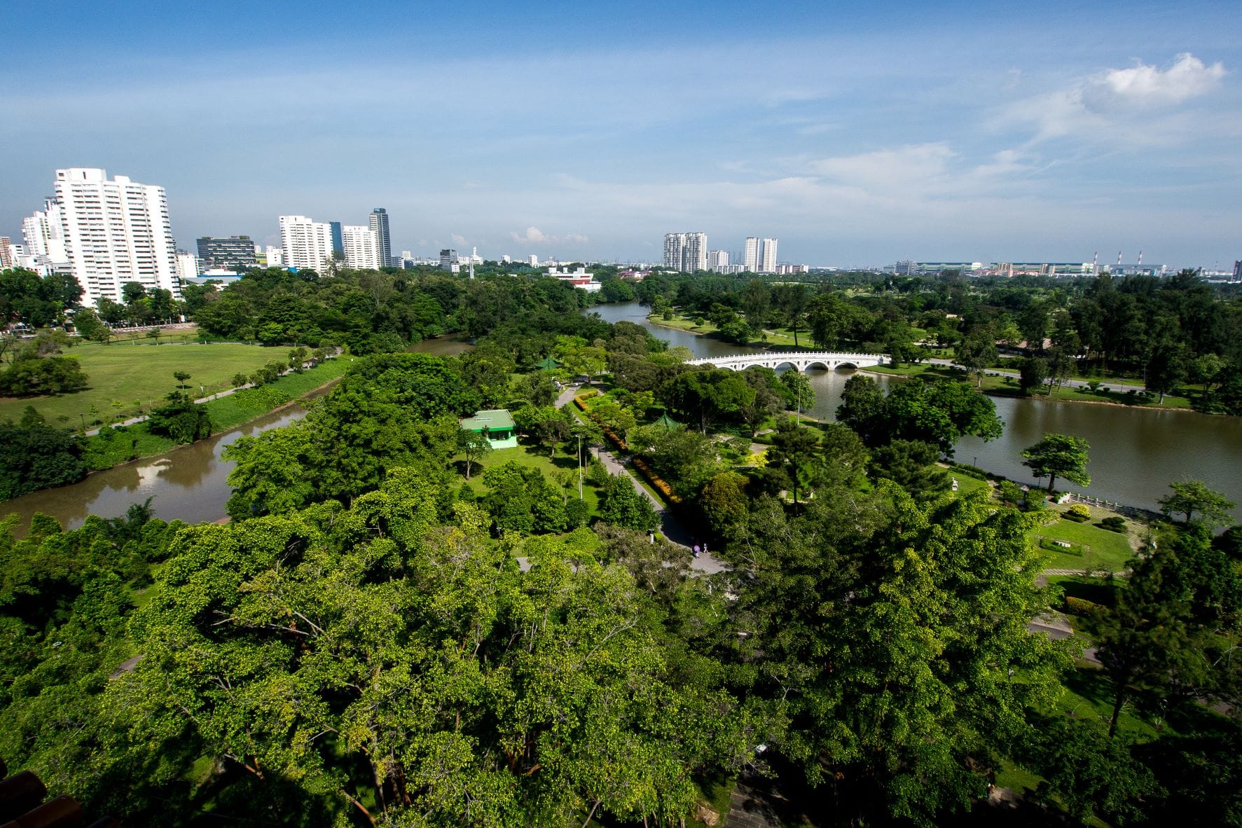 A cityscape featuring tall buildings in the background with a large park, river, and bridge in the foreground.